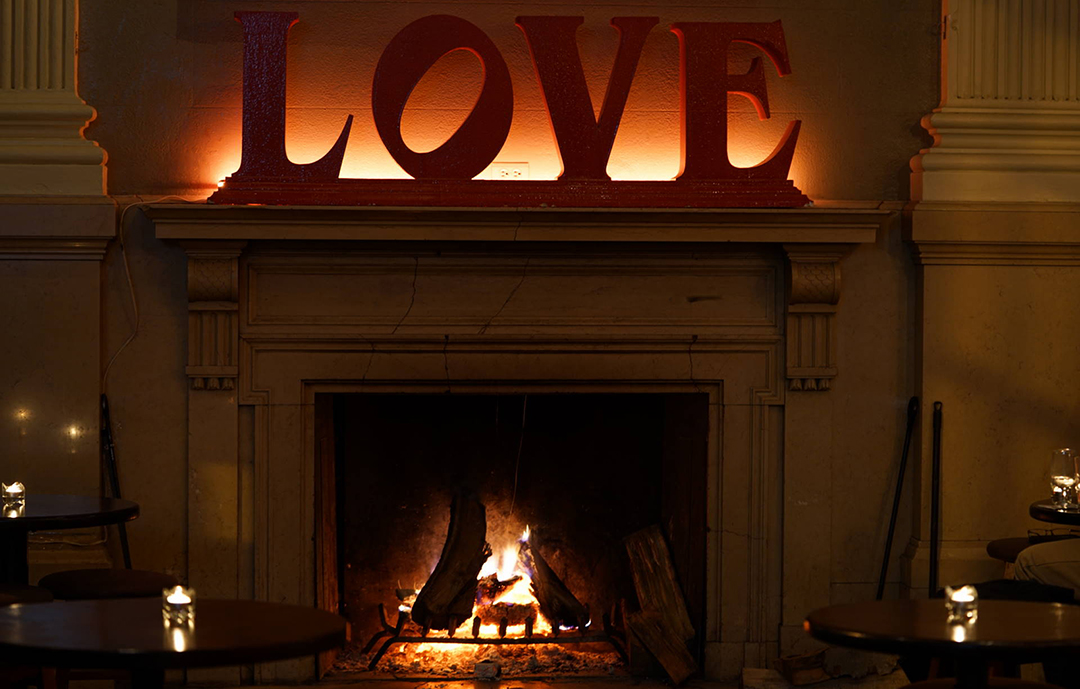 The warm open fireplace glowing beneath the neon LOVE sign at The Plough and The Stars